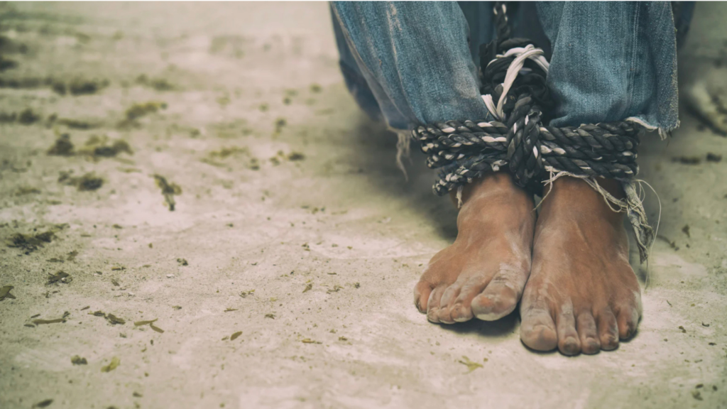 A person's feet tied up in sand, representing human trafficking and its various forms of coercion and exploitation.
